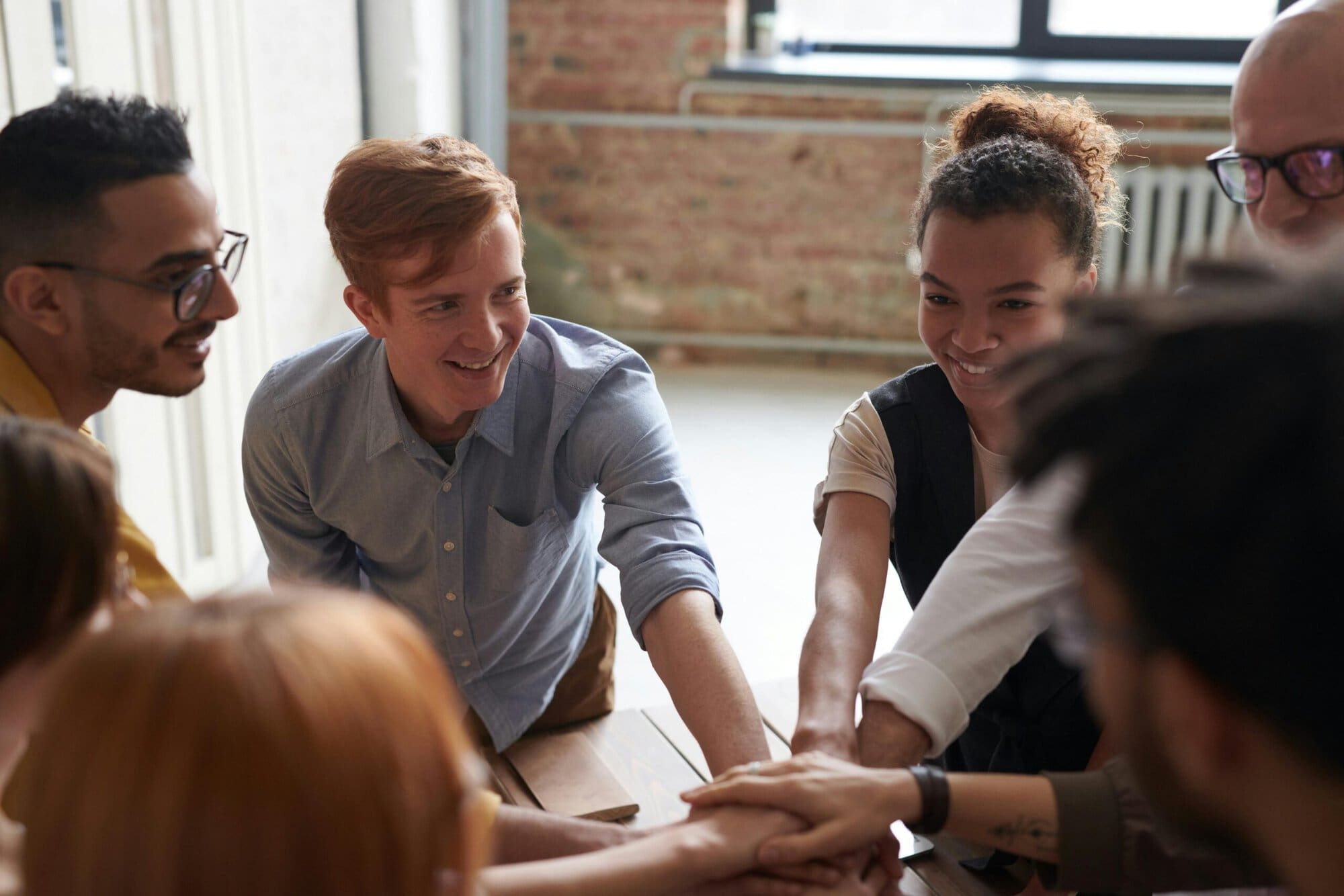 Ein diverses Team steht im Kreis und legt gemeinsam die Hände aufeinander, als Zeichen für Zusammenhalt und Zusammenarbeit.